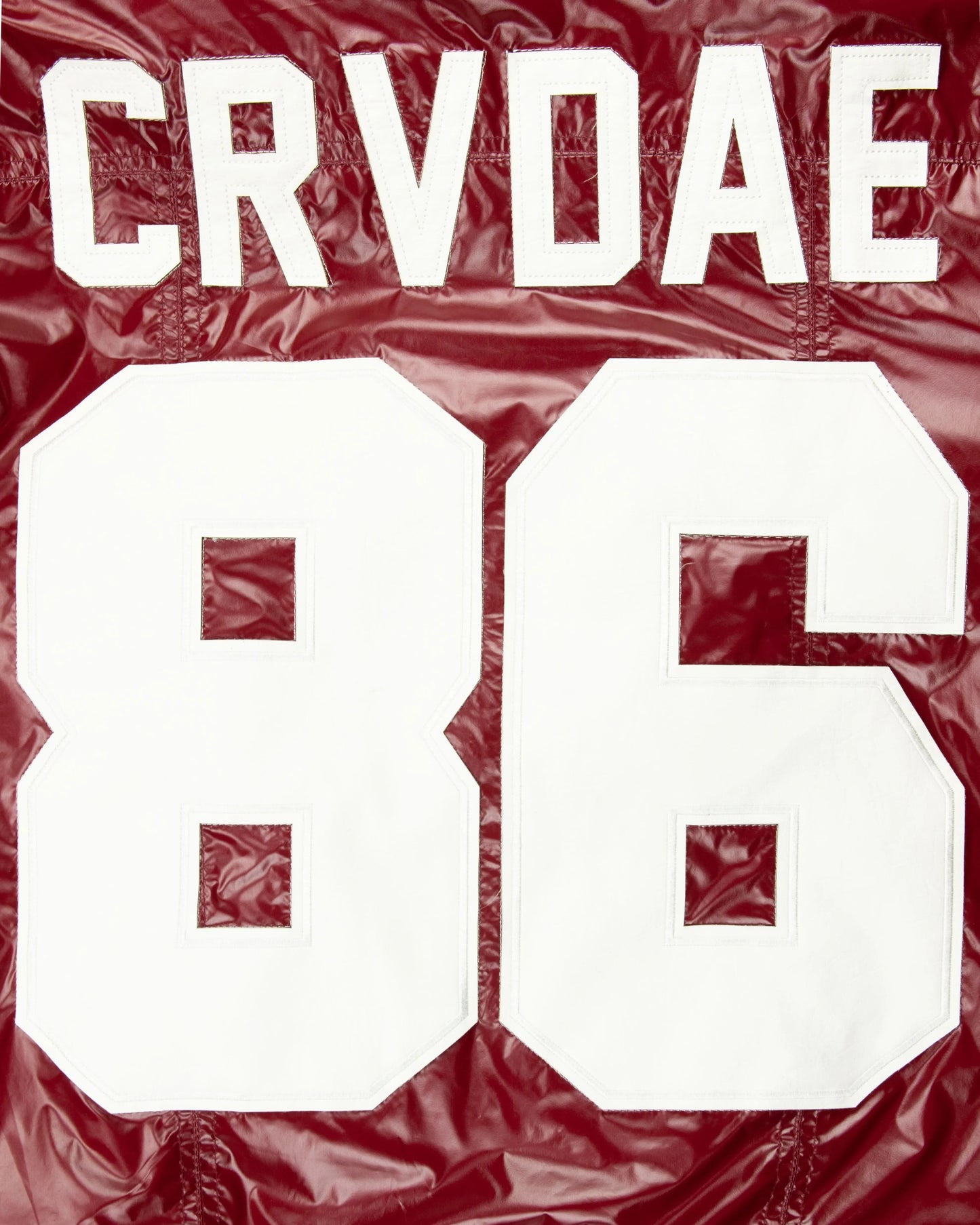 Close-up detail of the CRVDAE and 86 design on the back of a burgundy faux leather jacket, showcasing bold white lettering on a shiny finish.