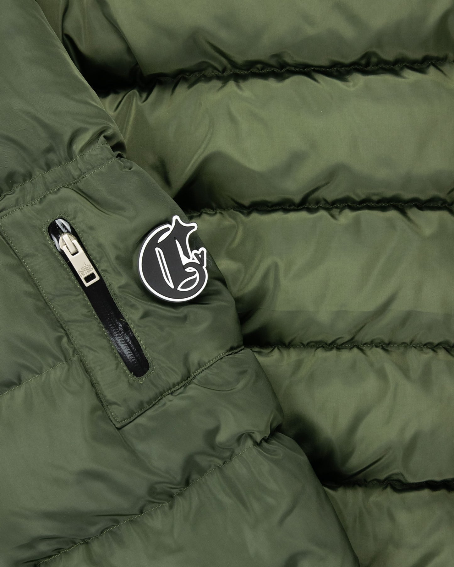 Close-up of detachable green puffer jacket sleeve with Corvidae C logo, zippered pocket, and quilted padding for functional and stylish outerwear.