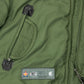 lose-up of men’s khaki green jacket highlighting front pocket design, black leather pull tabs, and embroidered label with logo details.