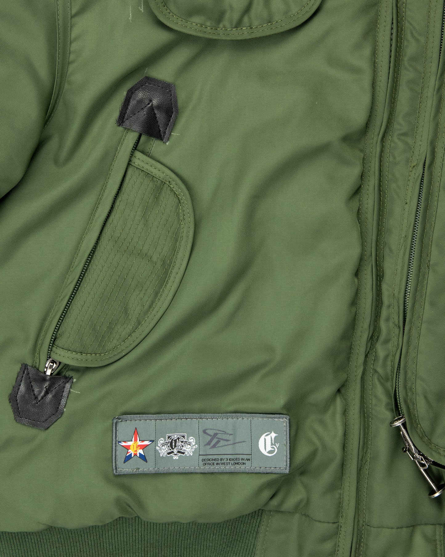 lose-up of men’s khaki green jacket highlighting front pocket design, black leather pull tabs, and embroidered label with logo details.