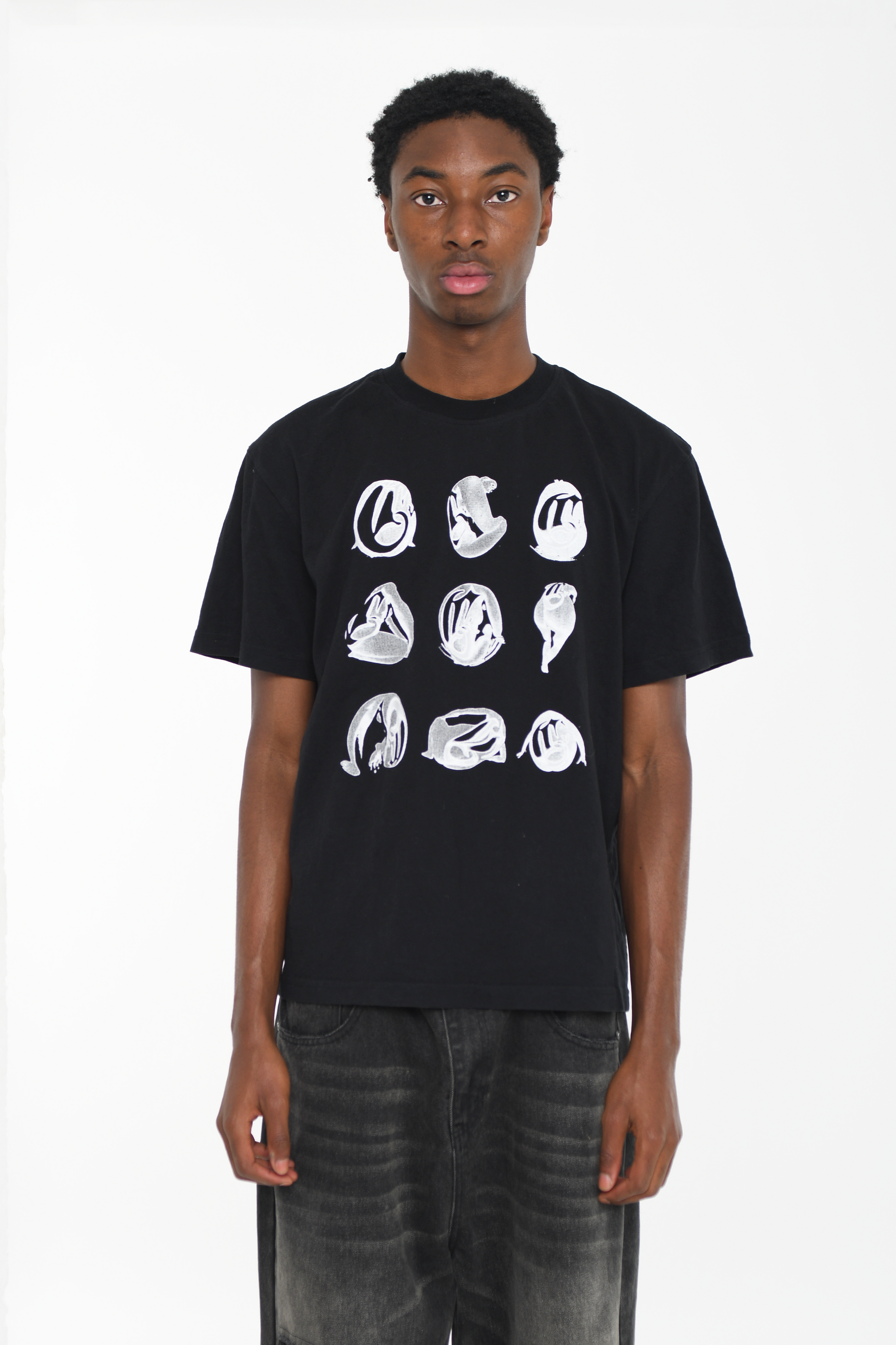 Male model wearing a black cotton T-shirt with a white abstract graphic design, styled for a contemporary casual outfit.