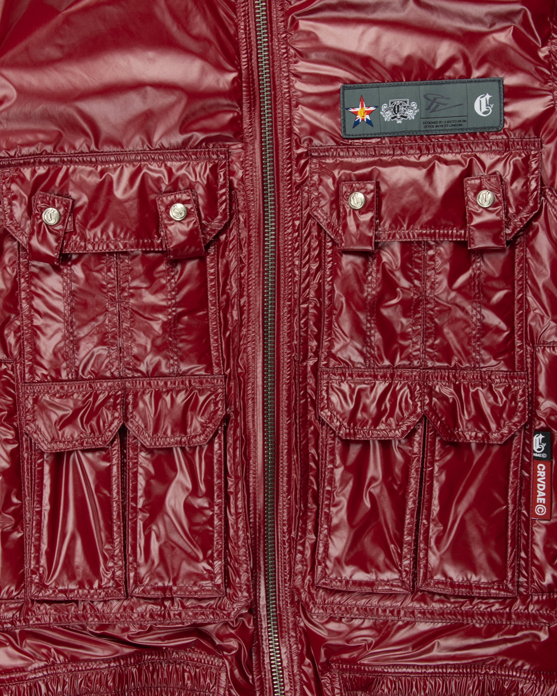 Close-up of the front pocket detail on a burgundy faux leather jacket, featuring multiple utility pockets, shiny finish, and CRVDAE branding.