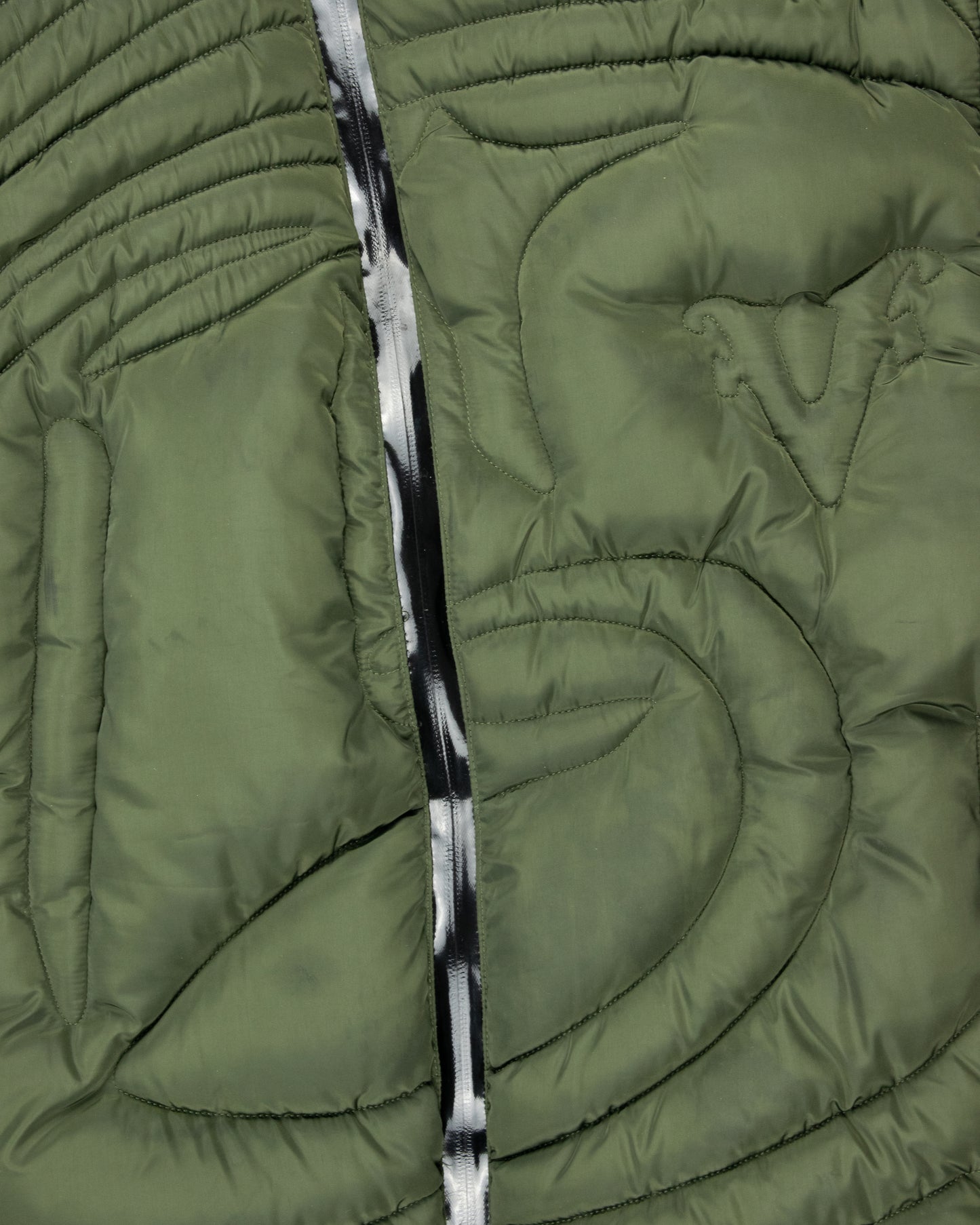 Close-up of the green embossed puffer jacket’s asymmetrical zipper and quilted stitching, highlighting modern craftsmanship and functional design.