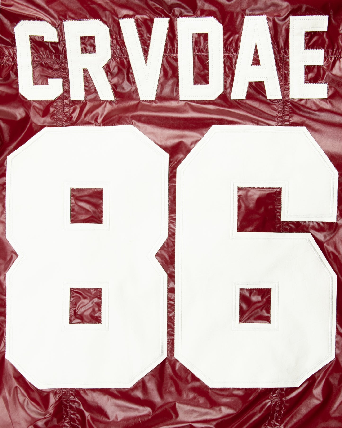 Close-up detail of the CRVDAE and 86 design on the back of a burgundy faux leather jacket, showcasing bold white lettering on a shiny finish.