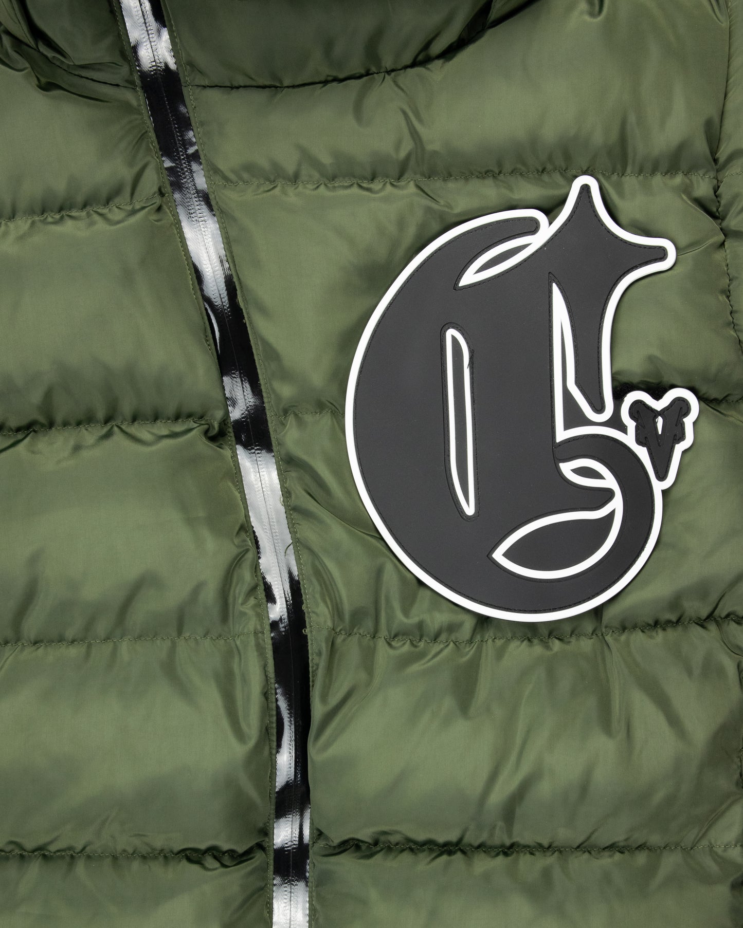 Close-up of detachable green puffer jacket featuring a bold Corvidae C logo and shiny black asymmetrical zipper design, showcasing modern streetwear style.