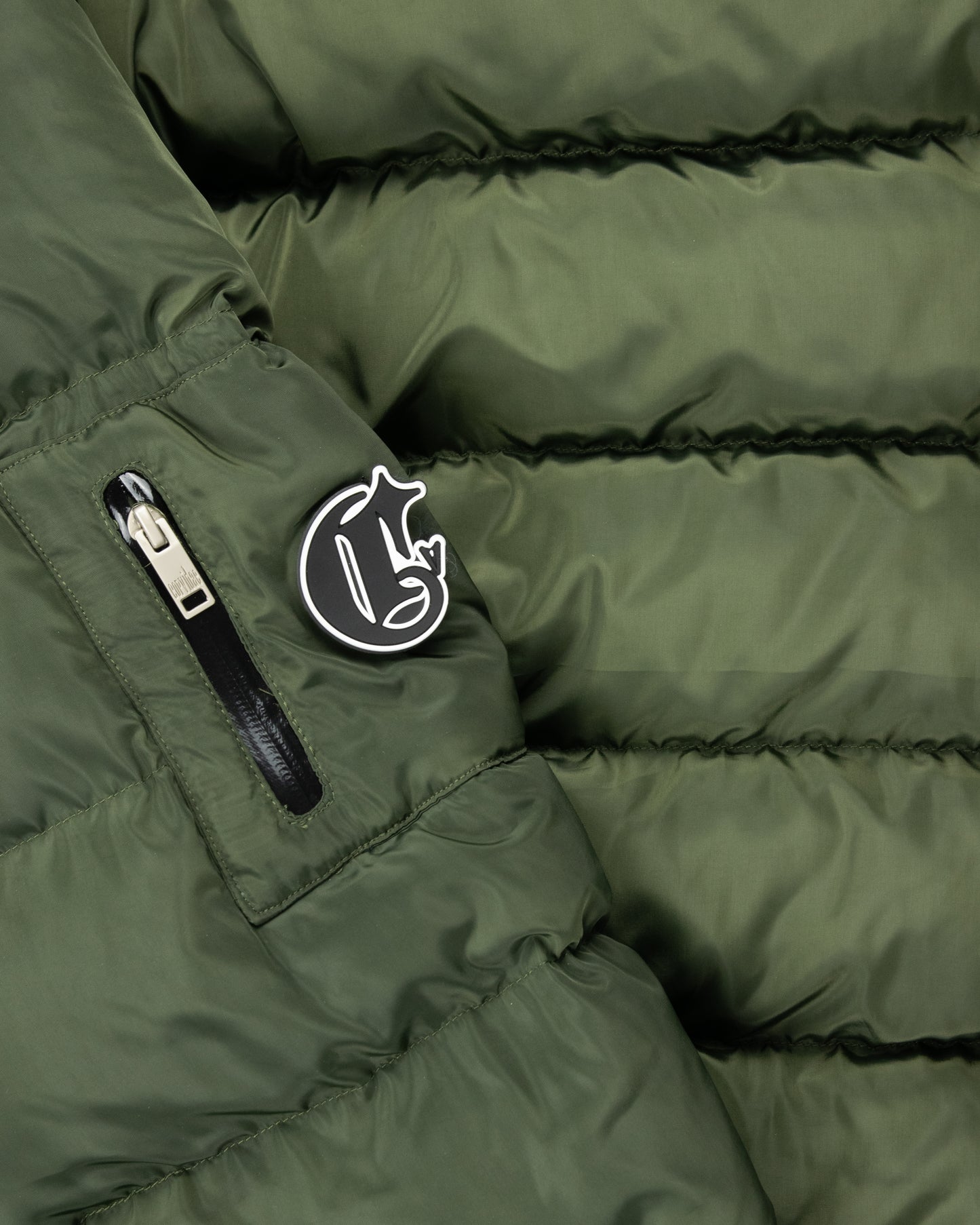 Close-up of detachable green puffer jacket sleeve with Corvidae C logo, zippered pocket, and quilted padding for functional and stylish outerwear.